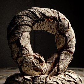 Buchcover „Baking Next Level mit Roggen“ mit dunkelrotem Hintergrund und rundem Roggenbrot in Nahaufnahme.