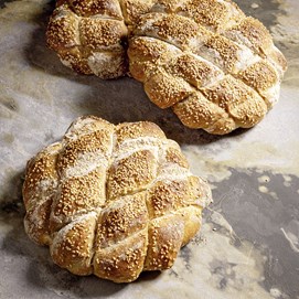 Buchcover „Baking Next Level mit Roggen“ mit dunkelrotem Hintergrund und rundem Roggenbrot in Nahaufnahme.