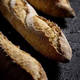 Buchcover „Baking Next Level mit Roggen“ mit dunkelrotem Hintergrund und rundem Roggenbrot in Nahaufnahme.
