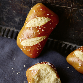 Buchcover „Brot backen in Perfektion mit Hefe“ mit Brotfotos und Porträt von Lutz Geißler auf dunklem Hintergrund.