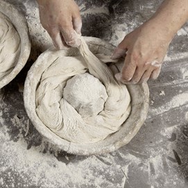 Buchcover „Baking Next Level mit Roggen“ mit dunkelrotem Hintergrund und rundem Roggenbrot in Nahaufnahme.
