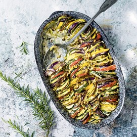 Buchcover „Deftig vegan mediterran“ mit goldbrauner Gemüsequiche, dekoriert mit Tomaten, Oliven und Kräutern.