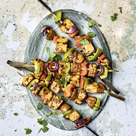 Buchcover „Deftig vegan mediterran“ mit goldbrauner Gemüsequiche, dekoriert mit Tomaten, Oliven und Kräutern.